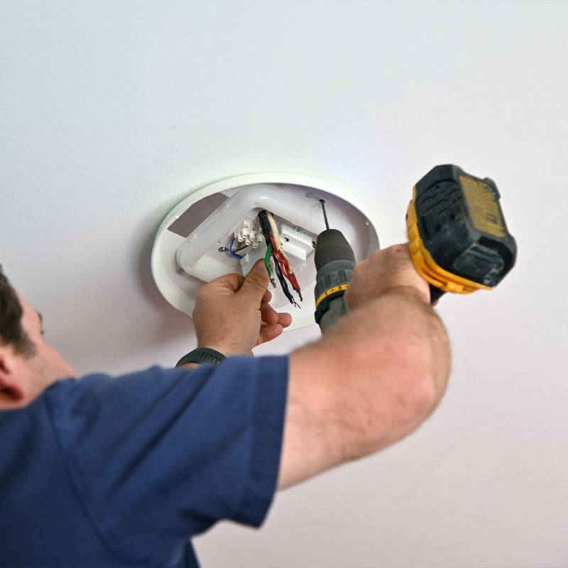 Man installs ceiling light fixture using power drill.