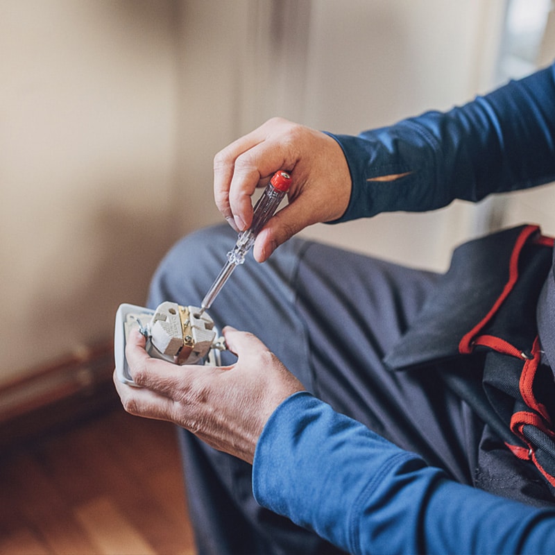 Electrician fixing a socket with a screwdriver, emphasizing professional electrical repair and maintenance work.