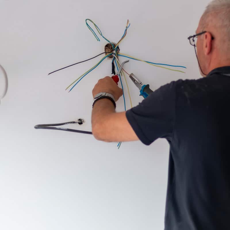 Electrician repairing ceiling wires using tools, ensuring safe electrical connections.