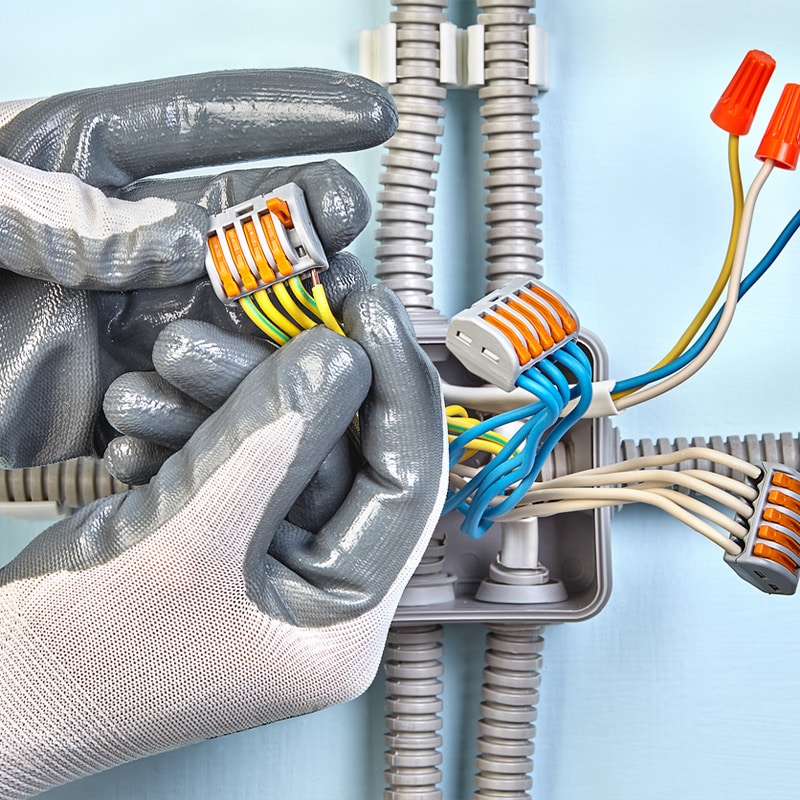 Electrician connecting wires in a junction box with protective gloves, showcasing wiring and safety equipment.