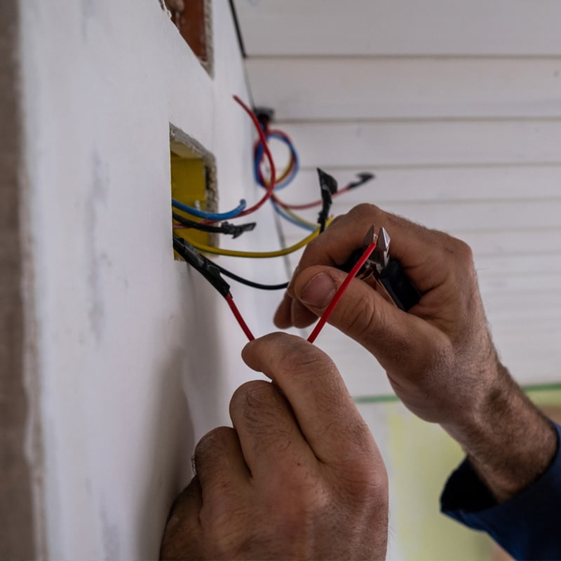 Electrician's hands wiring a socket, using pliers to connect colorful wires safely.