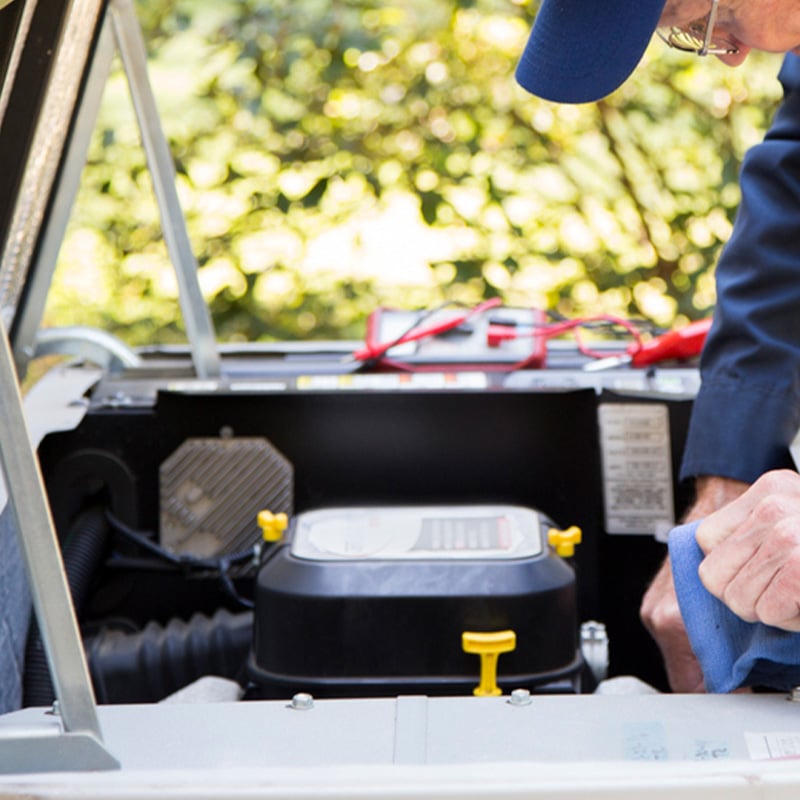 Technician servicing an outdoor backup generator in a garden setting.