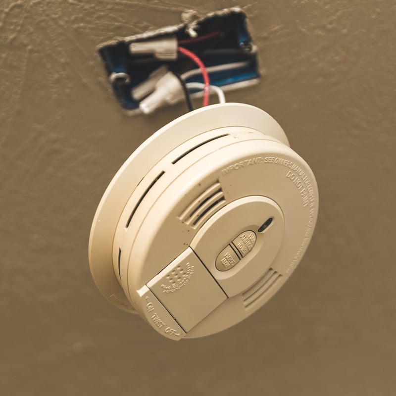Smoke detector installation on wall with exposed wiring for home safety.