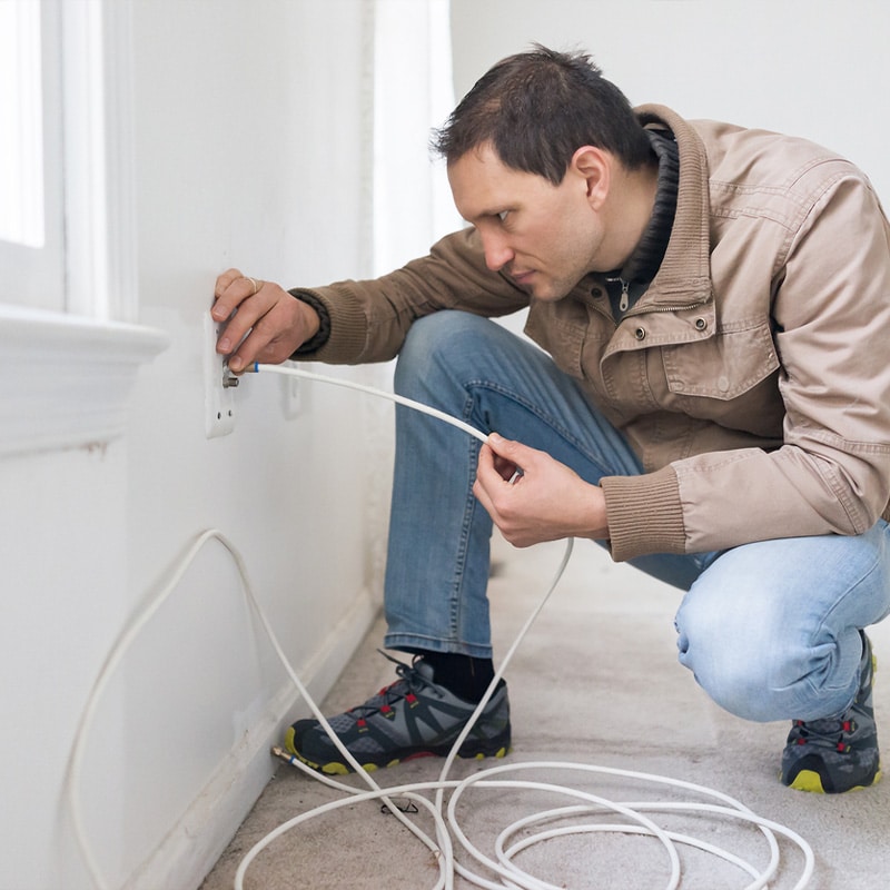 Man installing an Ethernet cable into a wall outlet in a home, focusing on internet setup and connectivity.