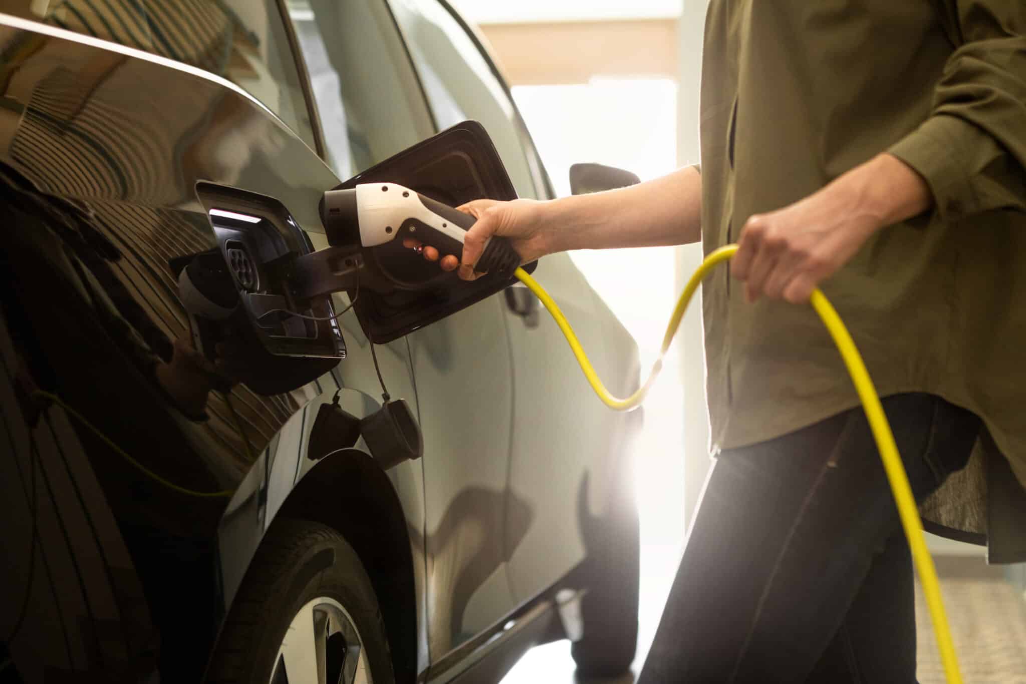 Person plugging an electric vehicle into a home EV charger in a garage.