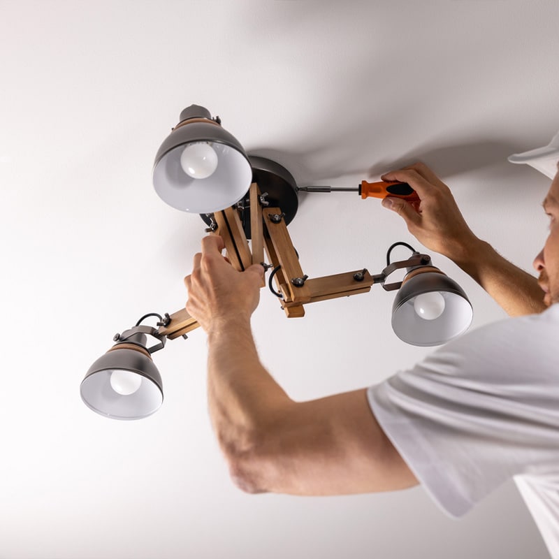 Man installing a ceiling light fixture with a screwdriver, adjusting modern wooden and metal lamp.