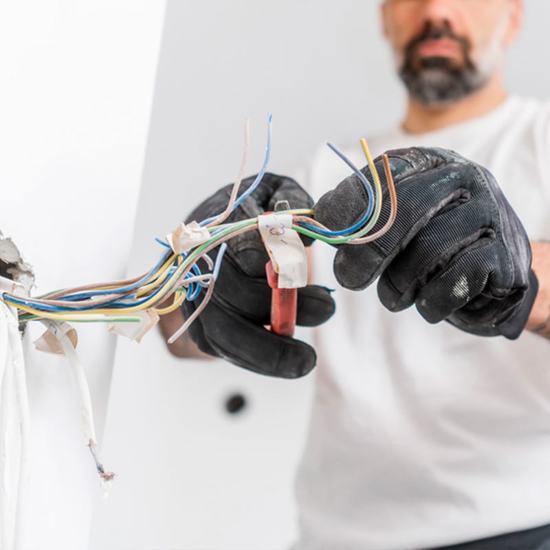 Electrician wearing gloves repairing electrical wires inside a wall for safety and maintenance.