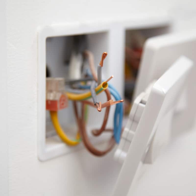 Close-up of exposed electrical wires in wall socket, highlighting safety and repair needs in home electrical systems.