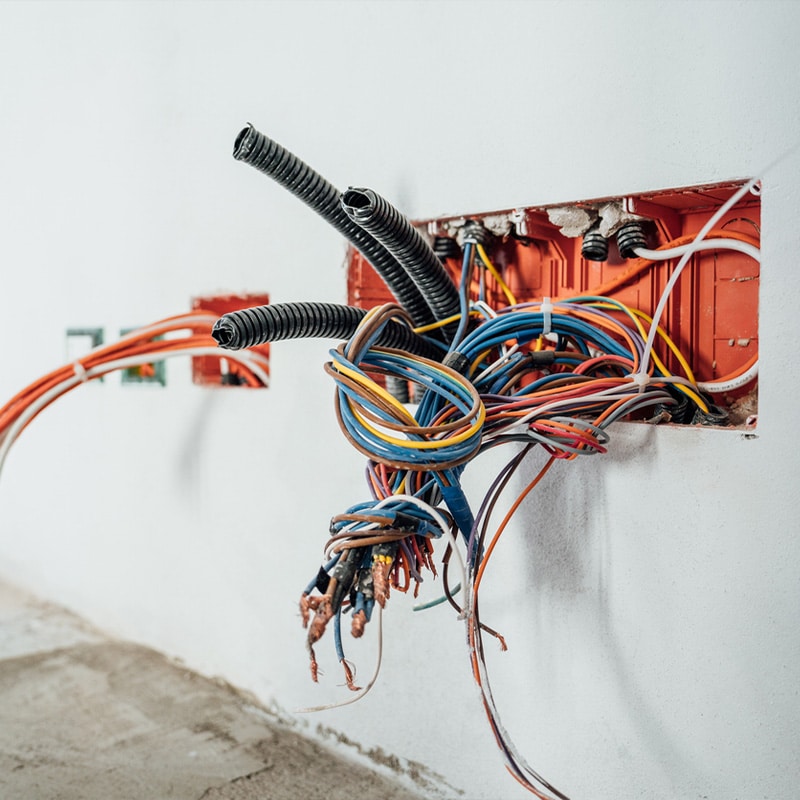 Tangled electrical wires and cables emerge from a wall outlet during home renovation work.