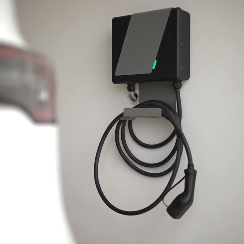 Wall-mounted electric vehicle charger with coiled cable, ready to charge a car.