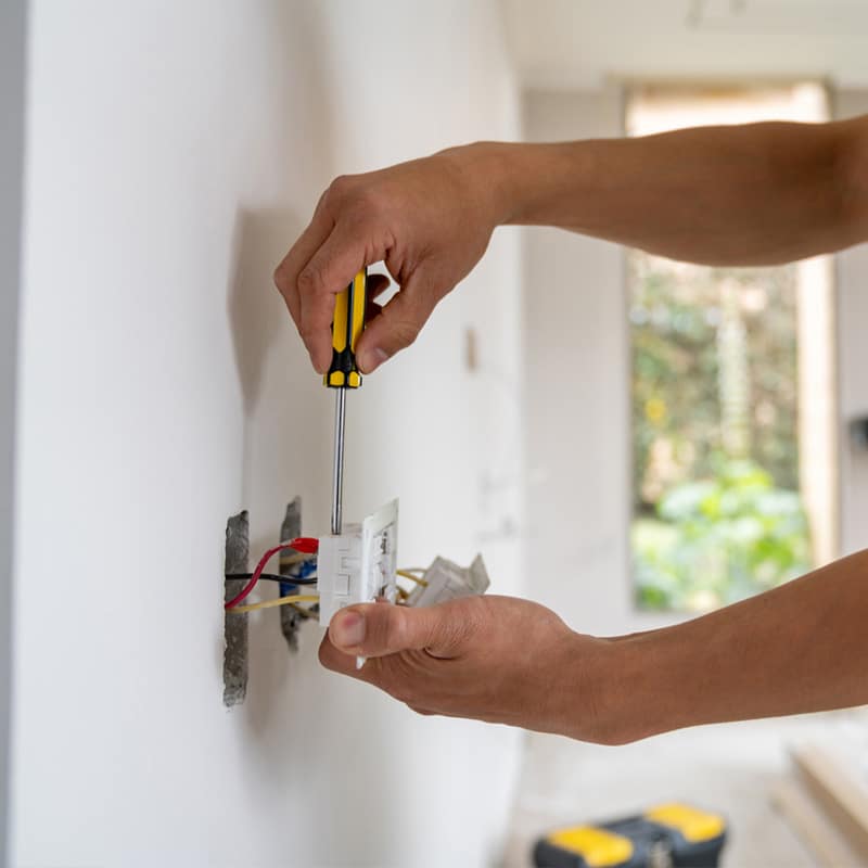 Electrician installing a wall socket with a screwdriver in a bright room.
