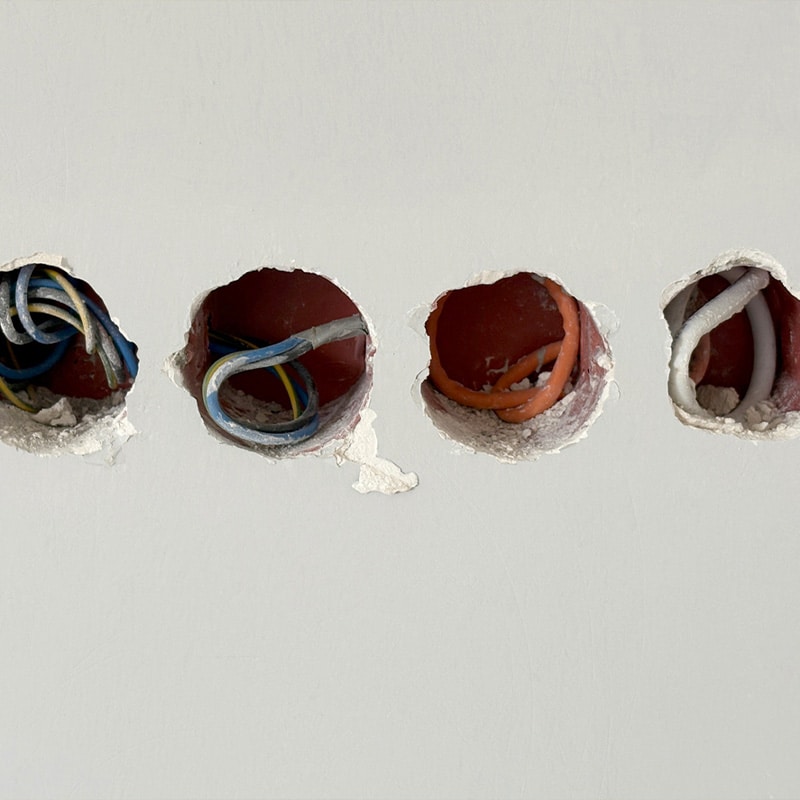 Close-up of electrical wiring through wall openings, showcasing various colored cables for installation or repair.