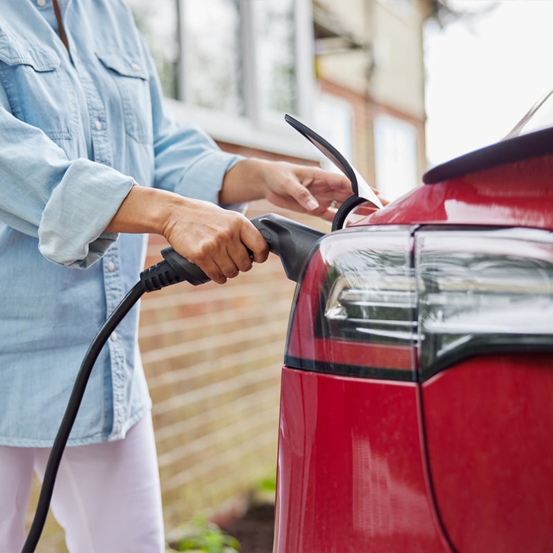 Person charging red electric car at home with a power cable, promoting sustainable transportation and green energy.