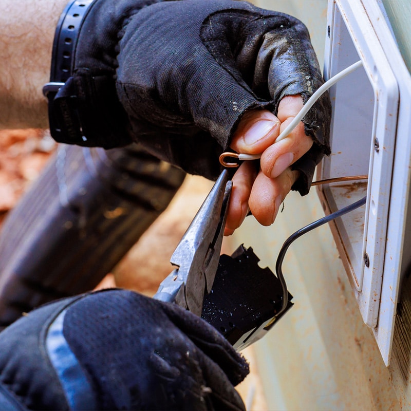 Electrician using pliers to install wiring on an outdoor electrical outlet for home improvement.