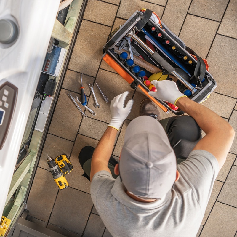 Technician organizing tools from a toolkit, surrounded by wrenches and a drill on tiled flooring.