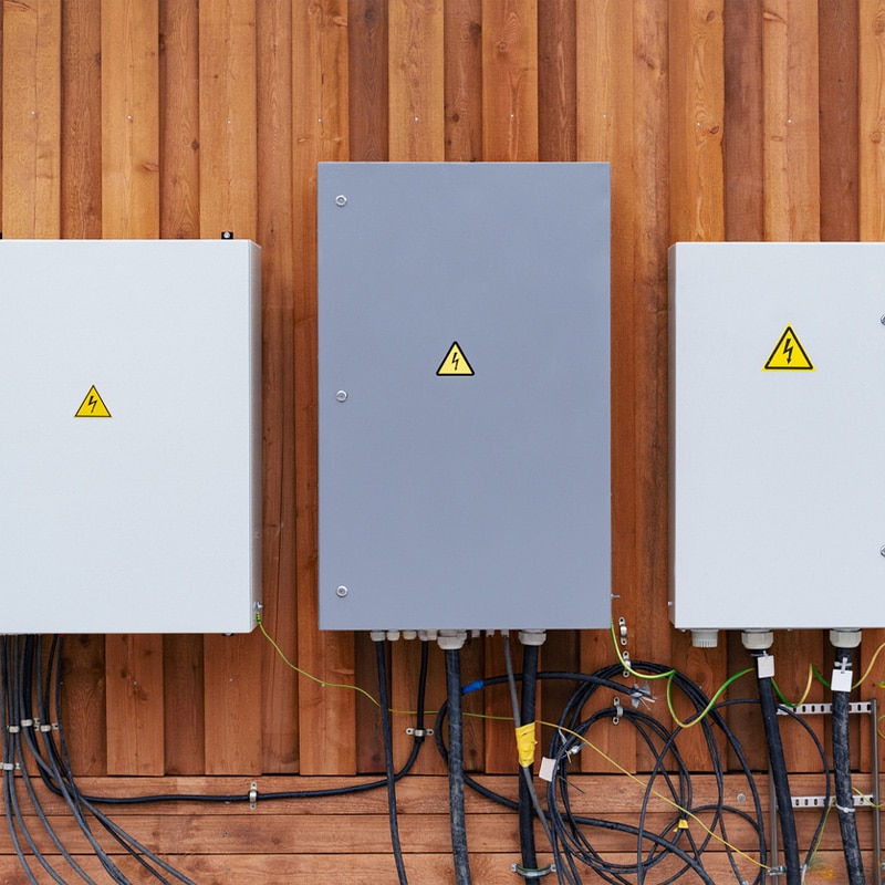 Electrical boxes with warning signs mounted on a wooden panel, showing connected cables.