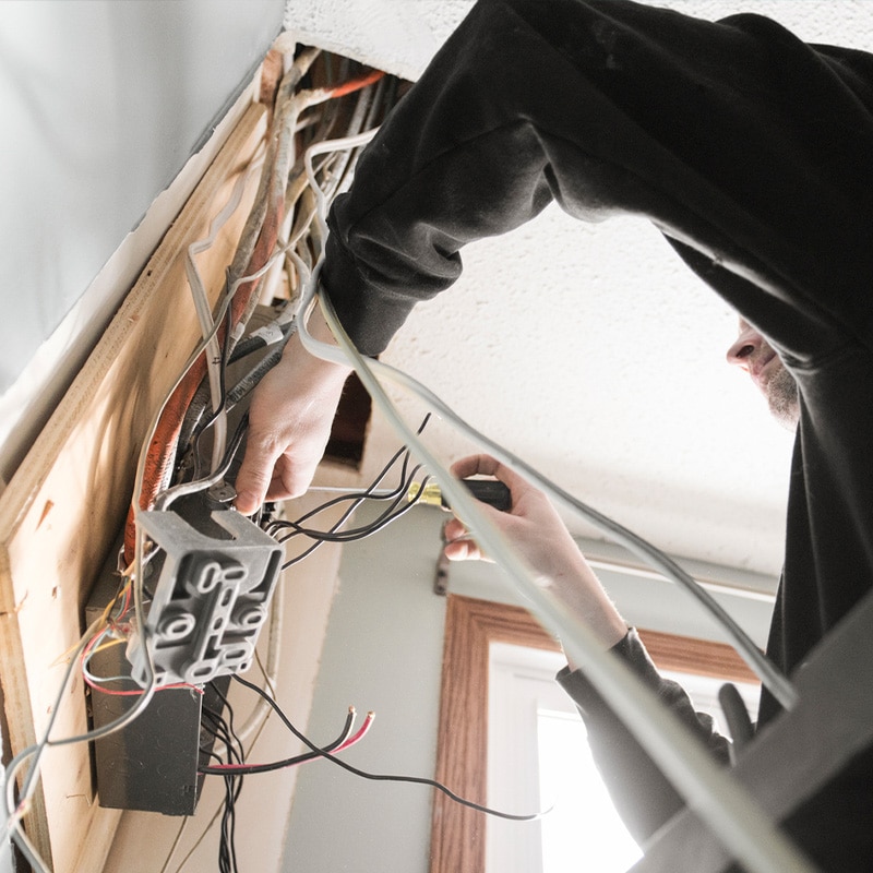 Electrician wiring a panel in a residential space, handling various cables for installation.