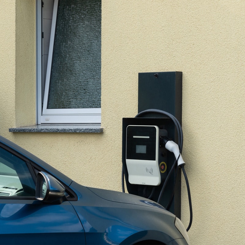 Electric vehicle charging at home station on beige wall near window.