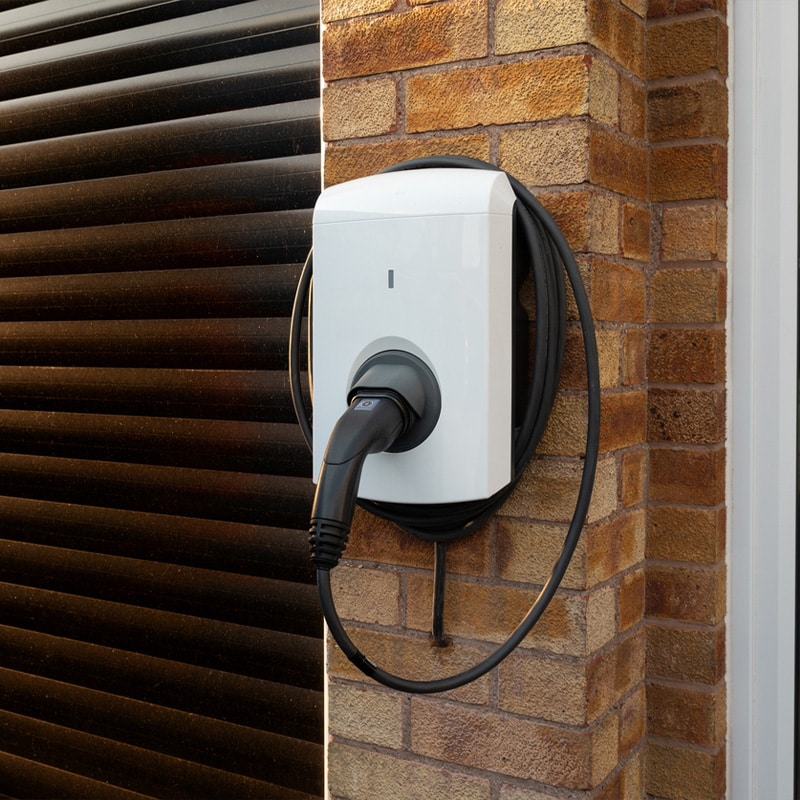 Electric vehicle charging station mounted on brick wall with black cable.